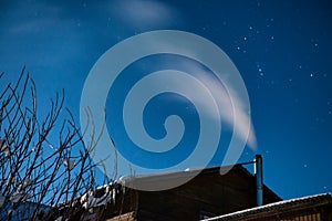 White smoke from the house chimney at the winter night sky background