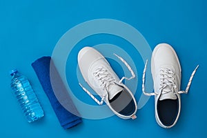White sneakers, a bottle of water and a blue towel on a blue background. Sports style. Flat lay.