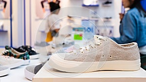 White sneakers on the display table in the fashion shoes store, close-up with blurred background of buyer. Costumers in shoes