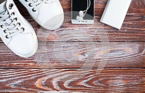 White sneakers, earphone with phone and charger on wooden background. Concept healthy lifestyle. Sports flatlay. Top view. Place