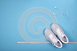 White sneakers with measuring tape and earphones headphones non blue background. n