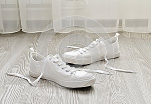 White sneakers with untied laces are on floor