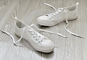 White sneakers with untied laces are on floor