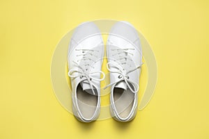 White sneakers on yellow background top view flat lay. Stylish youth women`s leather sneakers, sports shoes, genuine leather