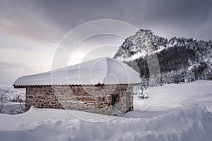 White snow covering a stone house under winter cloudy sky
