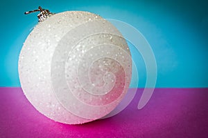 White snow small round xmas festive Christmas ball, Christmas toy plastered over sparkles on a pink purple blue background
