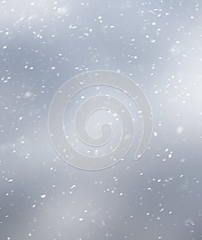 White snowflakes on a gray blurred inhomogeneous background, winter abstract background