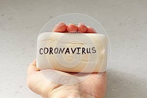 White soap lies in a female hand. Word coronavirus is written on soap. Concept of hand washing, hygiene, for prevention of