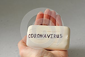 White soap lies in a female hand. Word coronavirus is written on soap. Concept of hand washing, hygiene, for prevention of