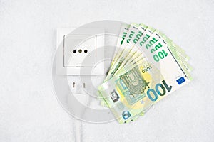 White socket with plug with many 100 Euro banknotes over light background. Concept of increasing prices for electricity in Europe