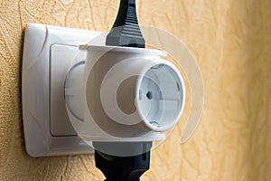 White socket on wall, closeup. Power cords cable plugged into european outlet.