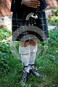 White socks. A man with a bagpipe, a kilt in a cage with a green and red stripe. Culture.The details of the skirt of the