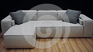 White sofa model with two gray pillows on a brown floor. Dark background. 4k video.