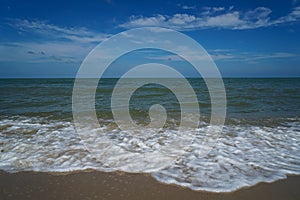 White soft foam of natural form sea wave on white sand beach with blue sky and white cloud background