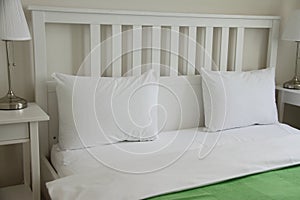 White soft pillows with green blanket on whte wooden bed