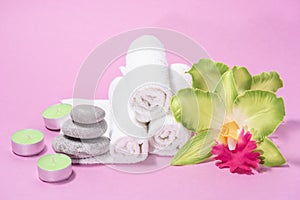 White soft terry towels, orchid, stones and candles for skin care and spa on a pink background