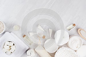 White spa cosmetics products and light bath accessories on white wood background, border, top view.