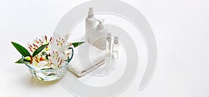 White spa towel with body care bottles and bowl with white lilies.