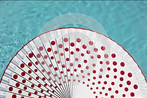 White spanish fan with red dots and swimming pool water behind