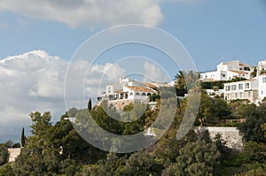 White spanish village on a green hill. White spanish houses surrounded by greenery against a blue sky. Mediterranean architecture.