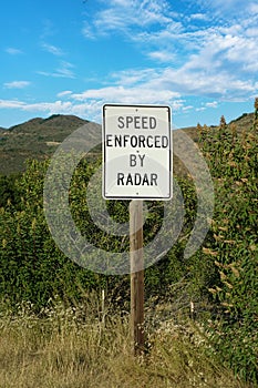 A white speed enforced by radar road sign alongside rural highway.