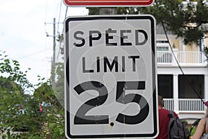 White speed limit sign on a road with trees behind it