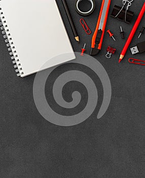 White spiral paper notebook with cutter knife, paper clumps, paper clips, push pins, colored pencils on dark background