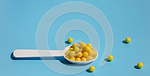 A white spoon filled with yellow vitamin C tablets on a blue background. Prevention of colds and flu.