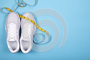 White sport shoes sneakers with measuring tape on blue background.