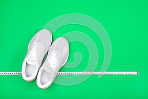 White sport shoes sneakers with measuring tape on bright green background.