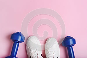 White sport sneakers shoes and blue dumbbells on the pink background.