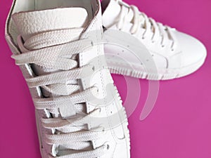 White sports sneakers with laces on pink background