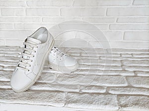 White sports sneakers with laces on white brick background