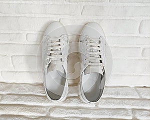 White sports sneakers with laces on white brick background