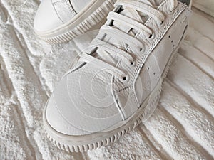 White sports sneakers with laces on white brick background