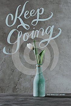 white spring tulip in blue vase and KEEP GOING lettering photo