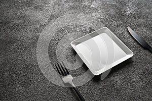 a white square empty plate, a black fork and knife. Stylish dinnerware for desserts. table setting. Suitable for