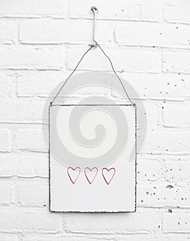 White square metal plate with cute red hearts and space for own text on white brick background