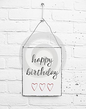 White square metal plate on white bricks background - with text happy birthday