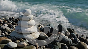White stack of stones in zen style stands next to coming sea waves. Sunny day at seaside.