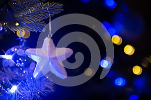 White star hanging on a Christmas tree, Christmas ornaments at night blue and gold holiday lights