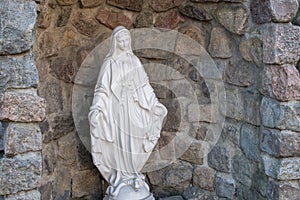 White statue of the virgin Mary in folds of clothing with bowed head, arms outstretched, trampling feet of serpent of tempte