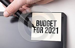 white sticker on the monitor in the office with text Budget for 2021 and hand with marker