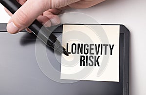 white sticker on the monitor in the office with text LONGEVITY RISK and hand with marker