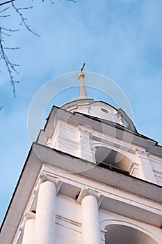 A white stone chapel of an orthodox chirch with a high golden cross going up to the sky. Low angle shot. Silhouette of branches