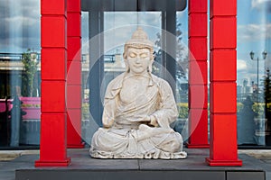 Sculpture of Buddha in meditative pose is located in the middle of red wooden columns
