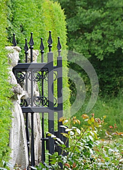 White stone sculptures at the entrance to the garden maze in Hever Castle park and black metal patterned gates on a blurred