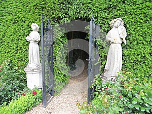 White stone sculptures at the entrance to the garden maze in Hever Castle park and black metal patterned gates on a blurred