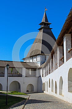 White stone wall of the courtyard with large arches and a wooden roof along the road. Historical and architectural complex