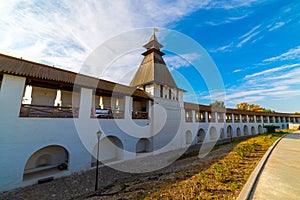 White stone wall of the courtyard with large arches and a wooden roof along the road with masonry in cloudy weather with blue